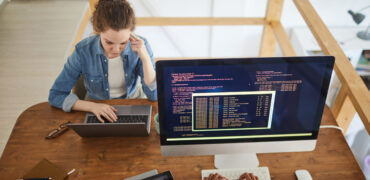 High angle portrait of young woman using laptop while working at desk in software development agency with unrecognizable male colleague writing code on computer screen in foreground, copy space